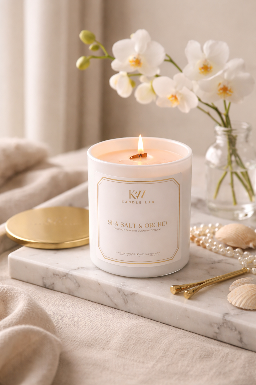 Candle with a decorative label on a marble surface with flowers and jewelry.