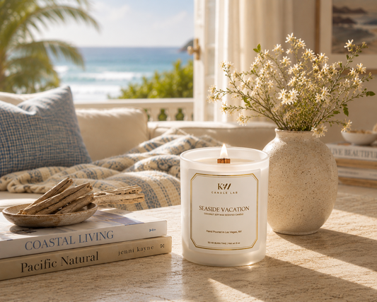 KW Candle Lab candle labeled 'Seaside Vacation' on a table with books and a vase of flowers, overlooking a beach.