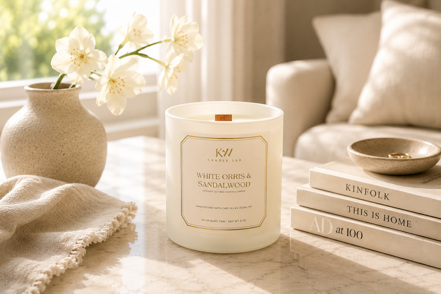 KW Candle Lab White Orris Sandalwood candlel on a table in a bright room with books and flowers.