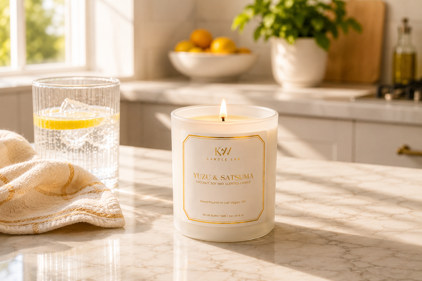 KW Candle  Lab yuzu satsuma scented candle on a kitchen counter with a glass of water and fruit bowl in the background