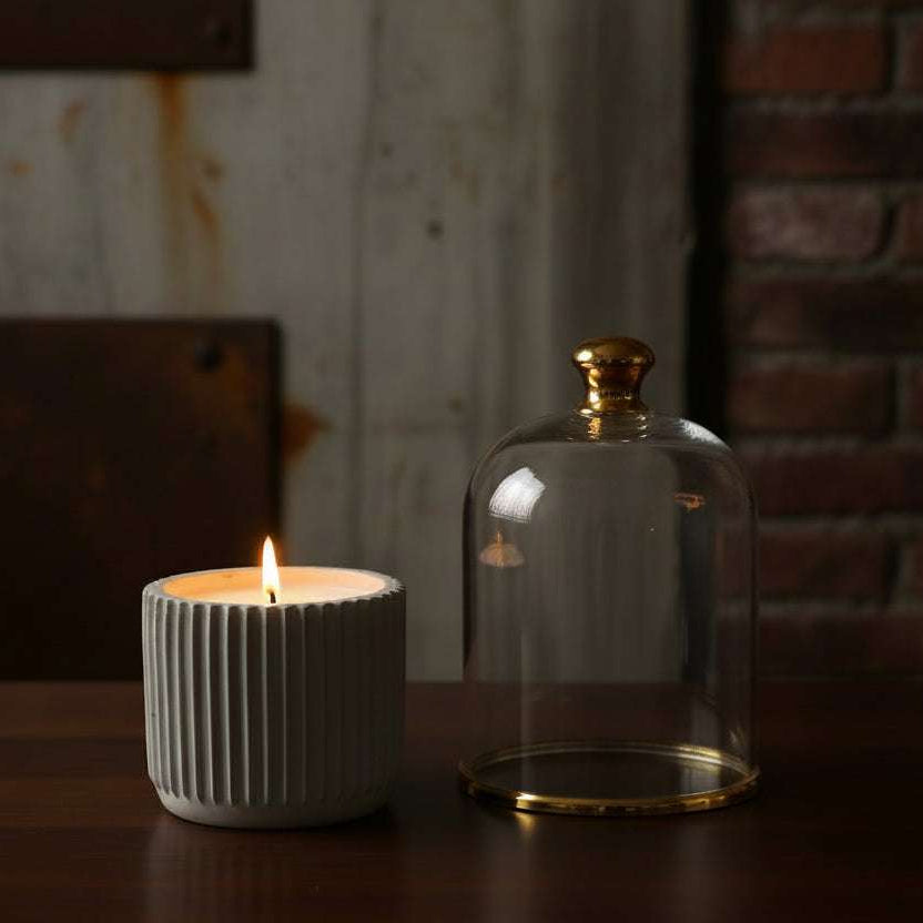 kw candle lab obsidian wood scented candle in a hand crafted concrete jar on a desk in a library next to a gold rimmed candle cloche