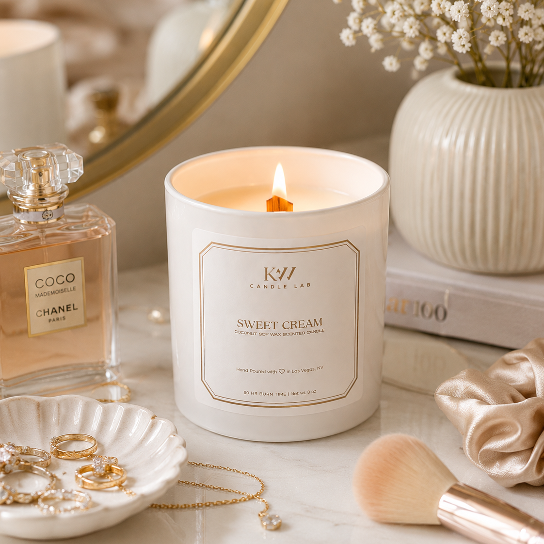 KW Candle Lab 'Sweet Cream' white candle lifestyle shot on a table with a mirror, flowers, and beauty products.